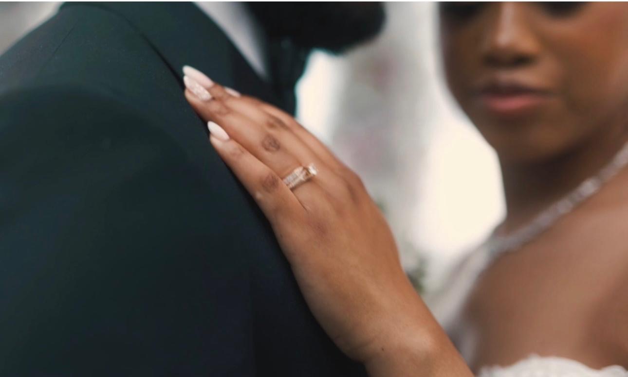 Bride's hand with her wedding ring resting on the groom's green tuxedo